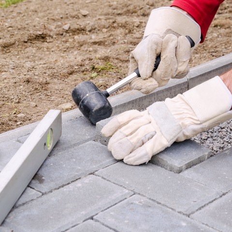 Bricklayer places concrete paving stone blocks for building up a pave patio, using hammer and spirit level. Handyman DIY concept.