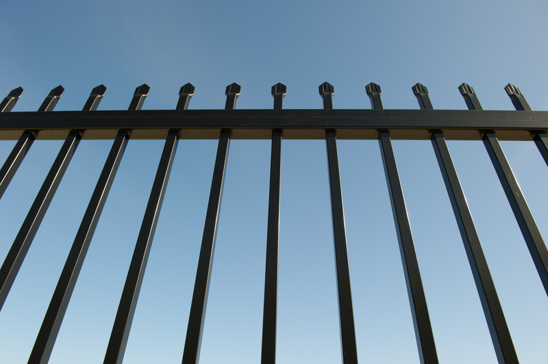 Security Fence around Industrial Property. Upward view of a metal security fence around an industrial property with spikes on top and a clear blue sky in the background.